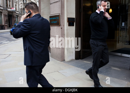 Deux hommes sur leurs téléphones portables passant sur un coin de rue. Banque D'Images