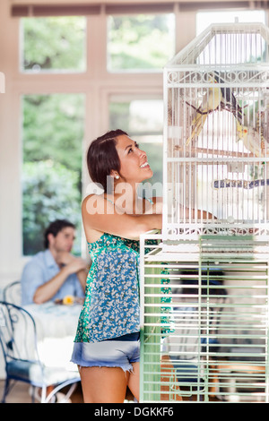 Femme debout par cage à oiseaux, l'homme en arrière-plan Banque D'Images