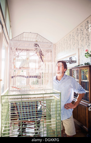 Portrait de jeune homme debout par cage à oiseaux et à la recherche au Parrot Banque D'Images