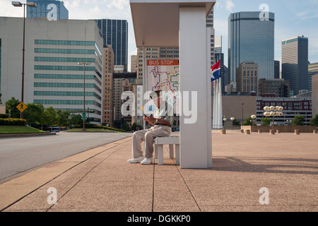 États-unis, Texas, Dallas, Senior man sitting at bus stop et de messagerie texte Banque D'Images