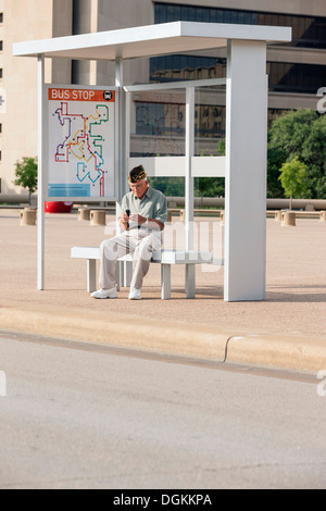 États-unis, Texas, Dallas, Senior man sitting at bus stop et de messagerie texte Banque D'Images