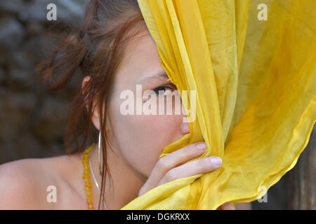Jeune femme se cachant derrière un foulard de soie jaune Banque D'Images
