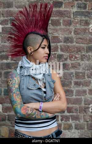 Une jeune femme avec bras tatoués et Mohican rouge style de cheveux pose pour la caméra à la London International Convention de tatouage. Banque D'Images