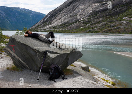 Femme portant des vêtements de randonnée couché sur un rocher sur le lac glaciaire de Jostedal, Nigardsbrevatnet Banque D'Images