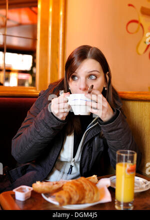 Jeune femme ayant le petit déjeuner avec croissants, baguette, jus d'orange et du café dans un café français, Paris, France, Europe Banque D'Images