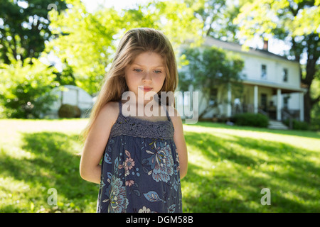 L'extérieur en été. À la ferme. Une fille dans le jardin avec ses mains derrière son dos. Banque D'Images