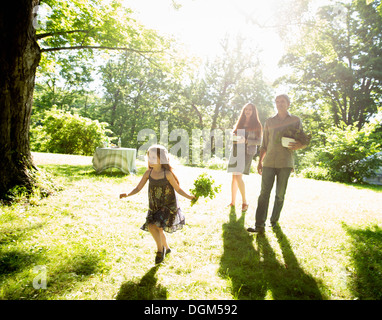 À la ferme. Deux adultes transportant des boîtes de légumes frais et de plantes. Une jeune fille transportant des bouquets d'herbes fraîches. Banque D'Images