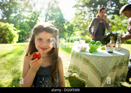 Une jeune fille tenant un grand produit biologique frais Fruits fraise. Deux adultes à côté d'une table ronde. Banque D'Images