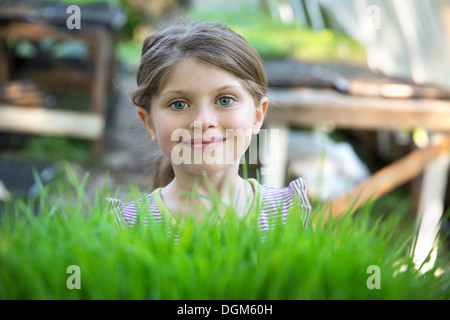 À la ferme. Une jeune fille souriant permanent par un banc en serre à plus de pousses vertes de la croissance des semis dans des bacs. Banque D'Images