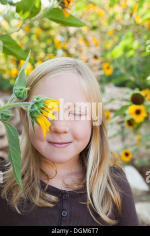 Un enfant debout dans un jardin de fleurs. Une fille avec les yeux fermés avec sun flower devant ses yeux. Banque D'Images