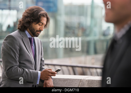 Deux hommes en costumes, sur une terrasse avec une balustrade. L'un contrôle de son téléphone. Banque D'Images