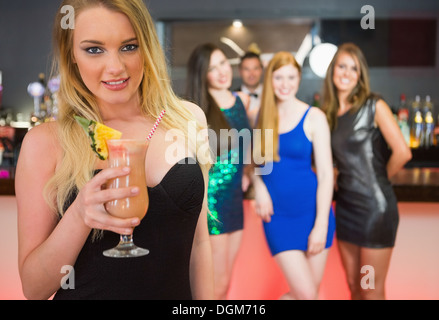 Jolie femme blonde holding cocktail debout devant ses amis Banque D'Images