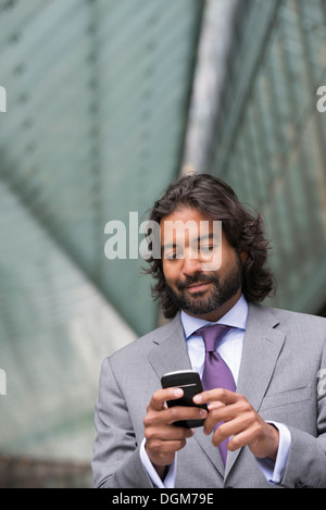 Les gens d'affaires. Un homme en costume avec une barbe et des cheveux bouclés. En utilisant son téléphone. Banque D'Images