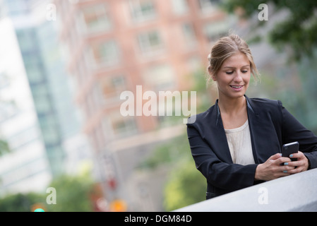 Une jeune femme blonde sur une rue de la ville de New York. Portant une veste noire. À l'aide d'un téléphone intelligent. Banque D'Images