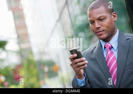 Un jeune homme dans un costume avec une chemise bleue et cravate rouge. Sur une rue de la ville de New York. À l'aide d'un téléphone intelligent. Banque D'Images