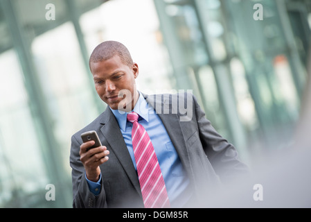 Un jeune homme dans un costume avec une chemise bleue et cravate rouge. Sur une rue de la ville de New York. À l'aide d'un téléphone intelligent. Banque D'Images