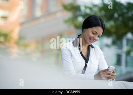 Les gens d'affaires. Une femme dans un manteau blanc contrôle de son téléphone. Banque D'Images