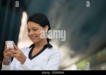 Les gens d'affaires. Une femme dans un manteau blanc contrôle de son téléphone. Banque D'Images