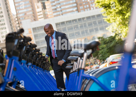 Les gens d'affaires. Un homme dans un costume d'affaires à côté d'un rack d'un service de location de vélos. Banque D'Images