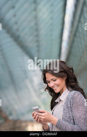 Les gens d'affaires. Une femme dans un manteau gris clair, à l'aide de son téléphone intelligent. Banque D'Images