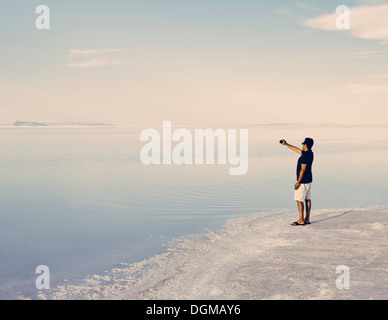 Un homme debout à bord de la Bonneville Salt Flats inondées au crépuscule, de prendre une photo avec un téléphone intelligent Banque D'Images