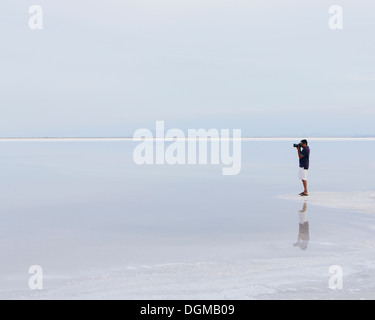 Un homme debout sur le bord de la Bonneville Salt Flats inondées, de prendre une photo au crépuscule. Banque D'Images