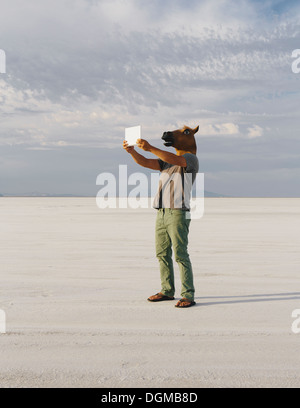 Un homme portant un masque de cheval, de prendre une photo avec une tablette, sur Bonneville Salt Flats. Banque D'Images