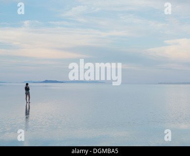 Une femme debout sur le Bonneville Salt Flats au crépuscule. Reflets dans l'eau peu profonde. Banque D'Images