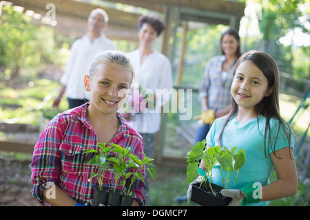 Ferme biologique. Fête de l'été. Deux filles assis tenant les jeunes plants, avec un couple d'âge mûr et une jeune femme à la recherche sur. Banque D'Images