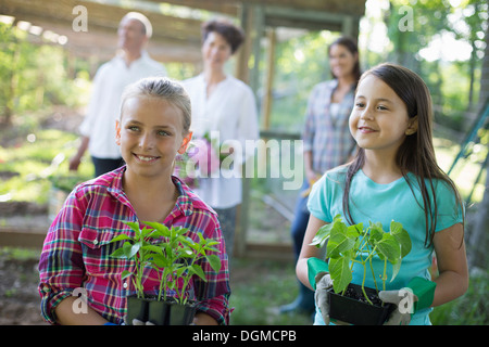 Ferme biologique. Fête de l'été. Deux filles assis tenant les jeunes plants, avec un couple d'âge mûr et une jeune femme à la recherche sur. Banque D'Images