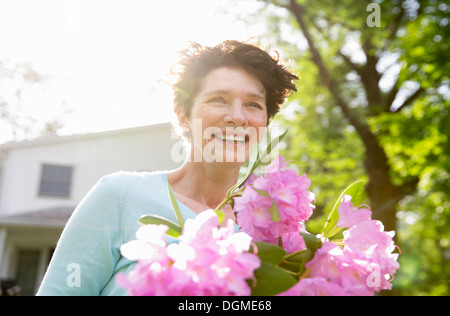 Partie de la famille. Une femme portant un gros bouquet de fleurs de rhododendron, souriant largement. Banque D'Images