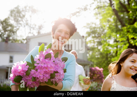 Partie de la famille. Une femme portant un gros bouquet de fleurs de rhododendron, souriant largement. Banque D'Images