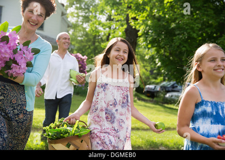 Partie de la famille. Les parents et enfants portant des fleurs, fruits et légumes frais cueillis. La préparation pour une fête. Banque D'Images