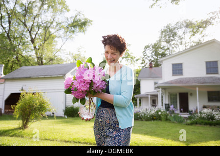 Partie de la famille. Une femme portant un gros bouquet de fleurs de rhododendron, souriant largement. Banque D'Images