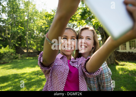 Deux filles assis dehors sur un banc, à l'aide d'une tablette numérique. Le tenant à bout de bras. Banque D'Images