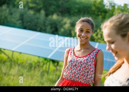 Deux jeunes filles à la ferme, à l'extérieur. Un grand panneau solaire à l'espace derrière eux. Banque D'Images