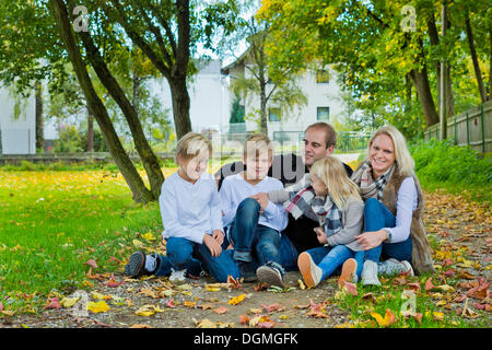 Famille avec trois enfants assis sur une prairie avec les feuilles d'automne Banque D'Images