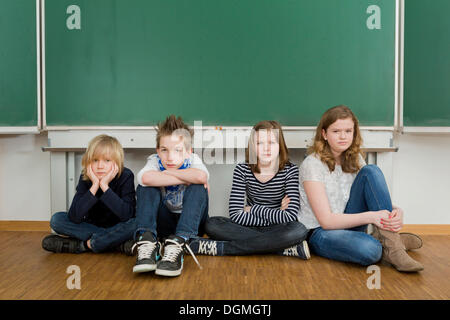 Les enfants de l'école s'ennuyer assis dans la salle de classe sur le sol à l'avant du tableau, Allemagne Banque D'Images