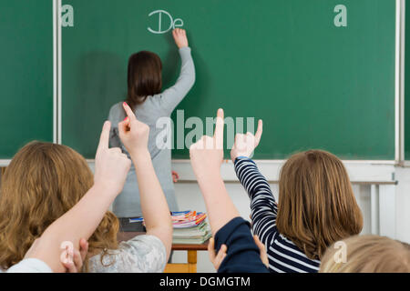 Les enfants de l'école levant les bras de répondre pendant la classe, Allemagne Banque D'Images