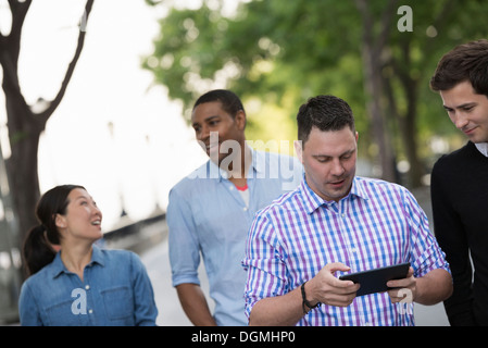 L'été dans la ville. Quatre personnes dans un groupe. L'un en utilisant sa tablette numérique. Banque D'Images