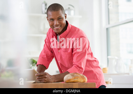Un jeune homme dans un chandail rose à l'aide d'une tablette numérique. Banque D'Images