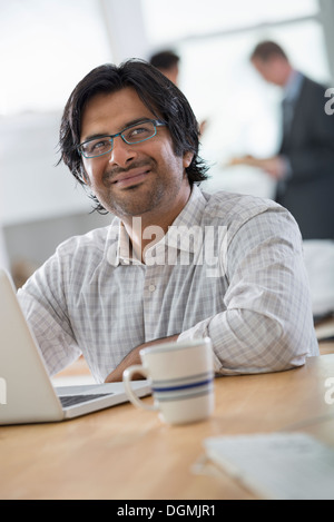 Un jeune homme dans un bureau à l'aide d'un ordinateur portable. Banque D'Images