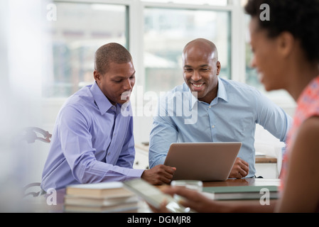 La vie de bureau. Trois personnes travaillant autour d'une table, à l'aide de tablettes numériques et ordinateurs portables. Banque D'Images