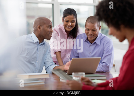 La vie de bureau. Quatre personnes travaillant autour d'une table, à l'aide de tablettes numériques et ordinateurs portables. Banque D'Images