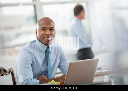 La vie de bureau. En homme d'une chemise et cravate assis à un bureau, à l'aide d'un ordinateur portable. Banque D'Images