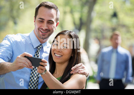 Un couple avec un téléphone intelligent, côte à côte. Un homme dans l'arrière-plan. Banque D'Images