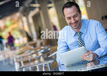 Un homme assis à l'extérieur à un café table à l'aide d'une tablette numérique. Banque D'Images