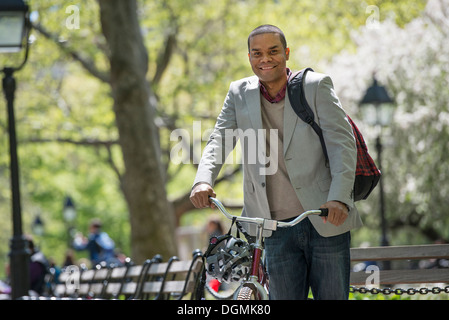 Une famille dans le parc sur une journée ensoleillée. Un homme poussant une bicyclette. Banque D'Images