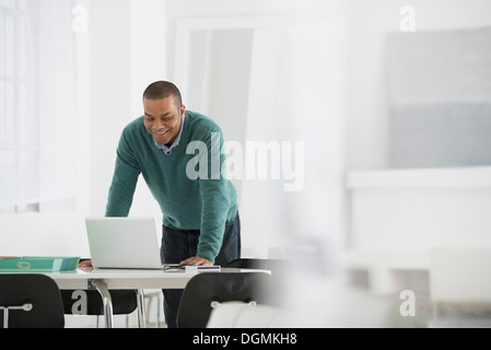 L'entreprise. Un homme debout sur un bureau, se penchant d'utiliser un ordinateur portable. Banque D'Images