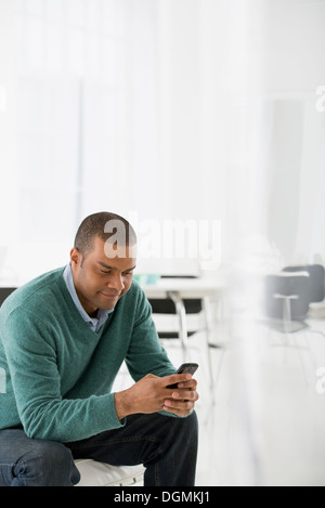 L'entreprise. Un homme assis, contrôler son téléphone intelligent pour les messages et les sms. Banque D'Images